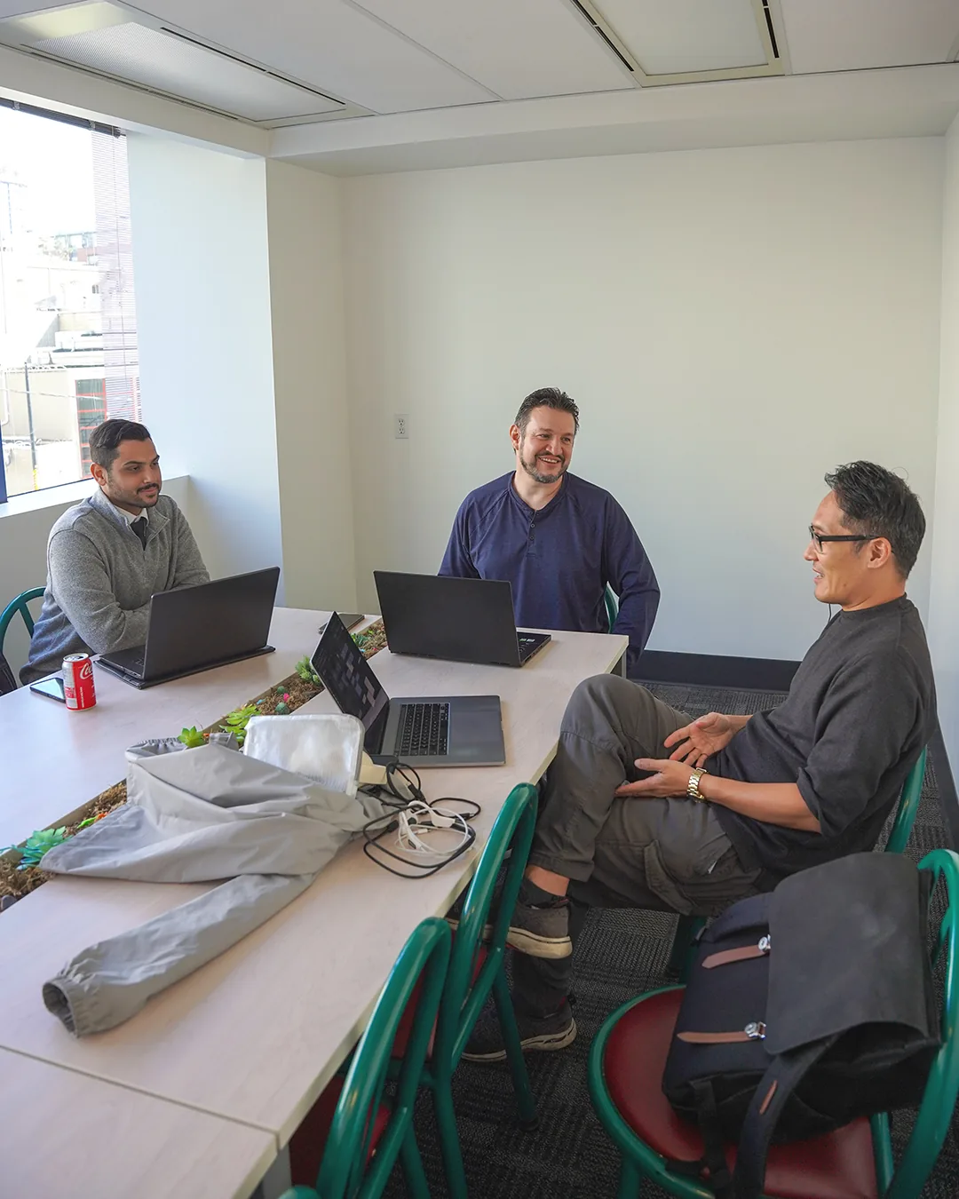 Three participants talking around a table with laptops.