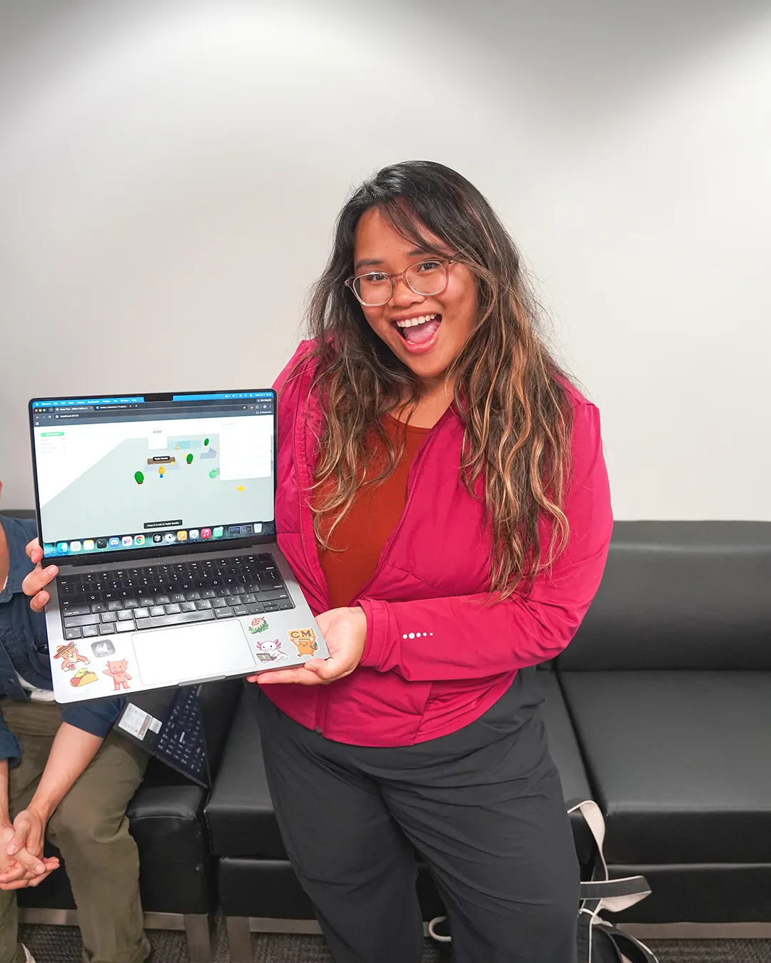 Charlene holding a laptop displaying her Don&rsquo;t Die In Office hackathon project.