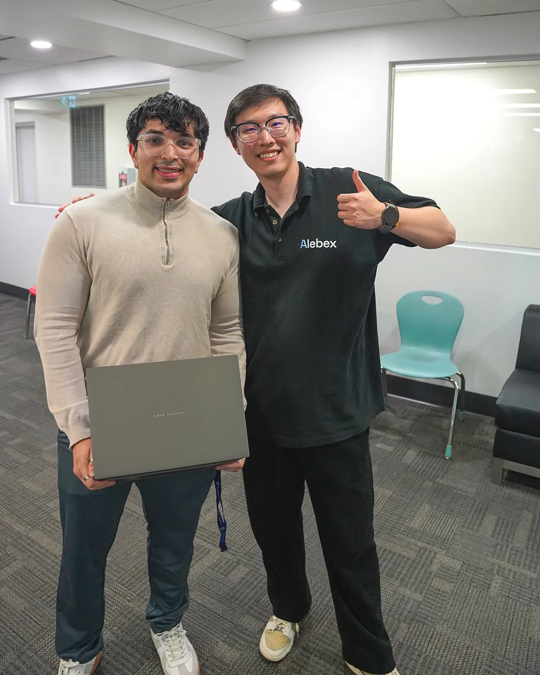 Two participants posing with a laptop at the hackathon.